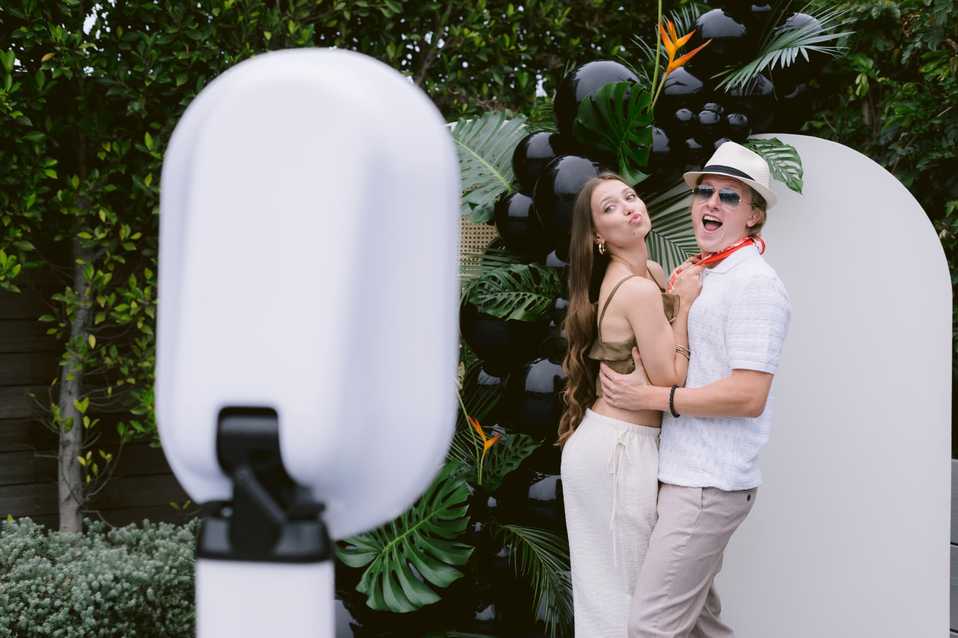 A couple posing in front of the photo booth and tropical backdrop